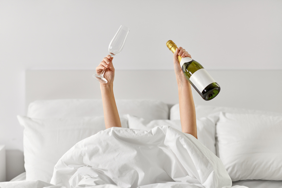Hands of Woman Lying in Bed with Champagne